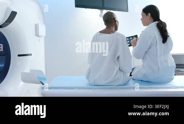 Two women, patient in gown, clinician sitting by scanner, showing ...