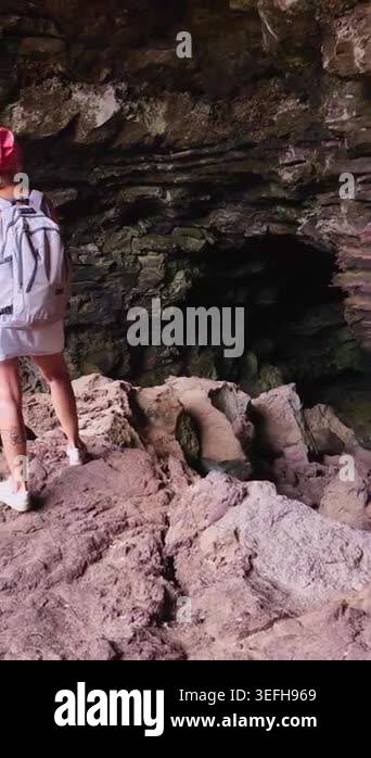Young female traveler with a backpack walking inside a dark volcanic ...