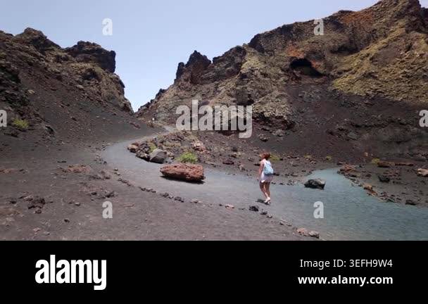 Young female traveler walking on volcanic black sand inside the crater ...