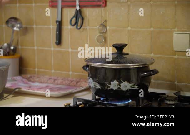 Woman lifting lid from boiling pot on gas stove with blue flame in ...