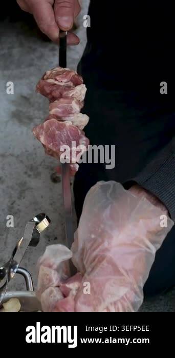 Gloved male hands are threading marinated pork pieces with onion onto ...