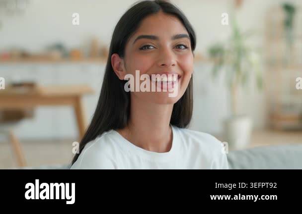 Happy smiling Indian Arabian Muslim woman looking at camera on sofa at ...