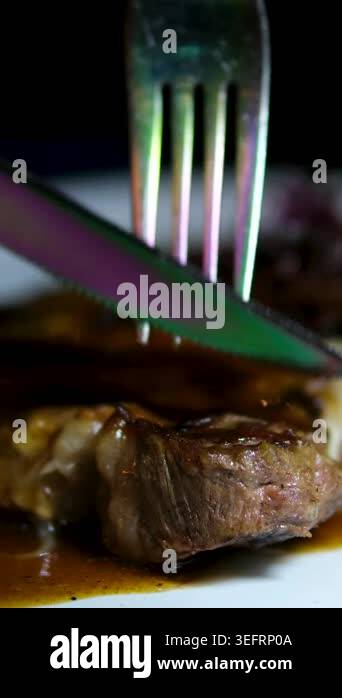 Tender rare steak on white plate in dim restaurant, rich sauce poured ...