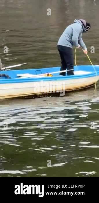 Two fishermen on a blue boat on Vltava river. One sits with a rod, the ...