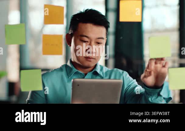 Man with dark skin stands in a bright office space, focusing on sticky ...