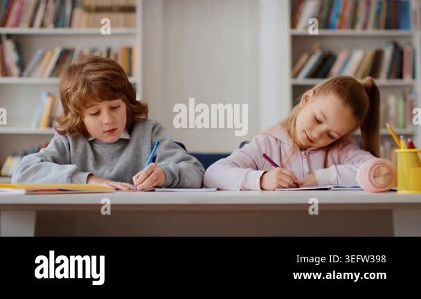 Two children, a boy with curly hair and a girl with long hair, sit at a ...