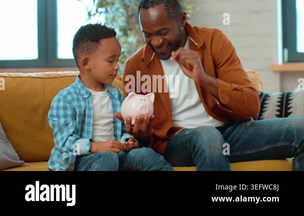 A man with dark skin is smiling as he shows a boy how to save money ...