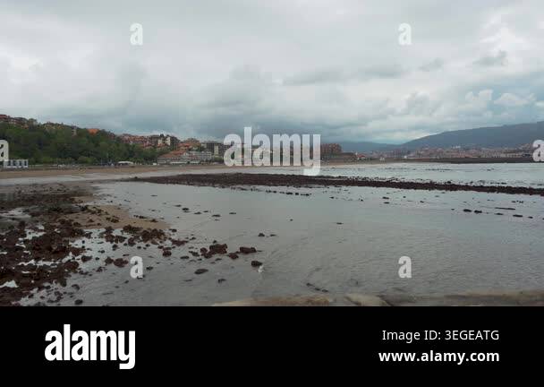 Dramatic cloudy sky over a coastal town with a rocky beach at low tide ...