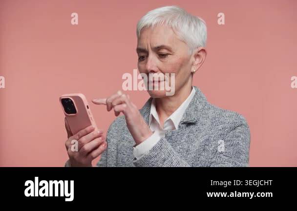 Focused senior woman with short white hair taps a smartphone screen ...