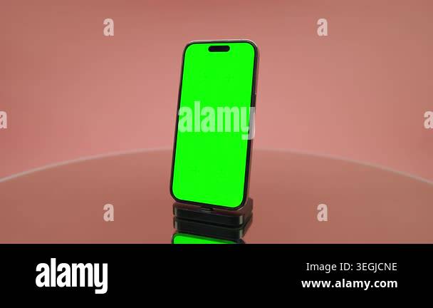Modern smartphone on a small stand with bright green screen, pink ...