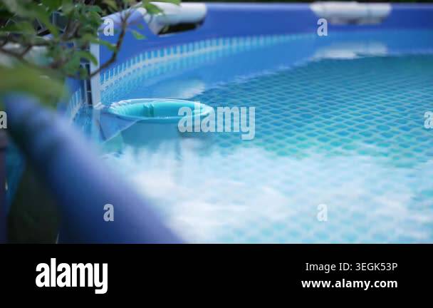 A pool skimmer floats quietly near the edge of a blue above-ground pool ...