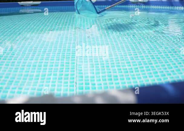 A pool skimmer net glides across clear blue swimming water. Ripples ...