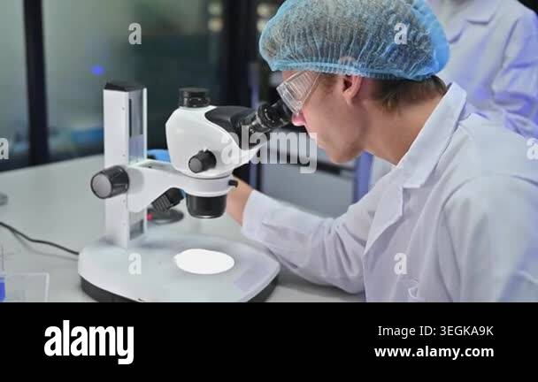 Professional male scientist wear safety goggles and hairnet examine ...