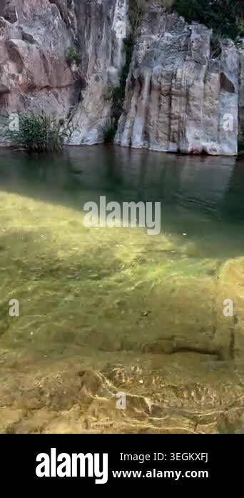 Transparent canyon pool with sun reflections, rocks, reeds, and small ...