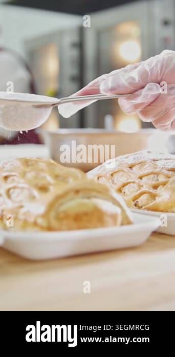 Hands in gloves sprinkle flour over freshly baked pastries placed on a ...