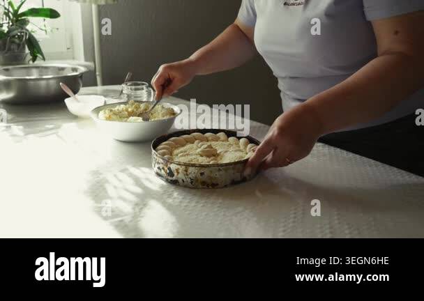 Woman layers dessert ingredients in a round baking dish on a kitchen ...