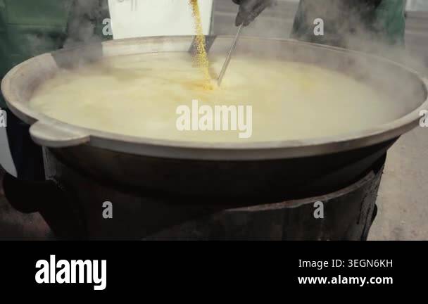 Yellow grains are poured into a large boiling pot, with steam rising ...