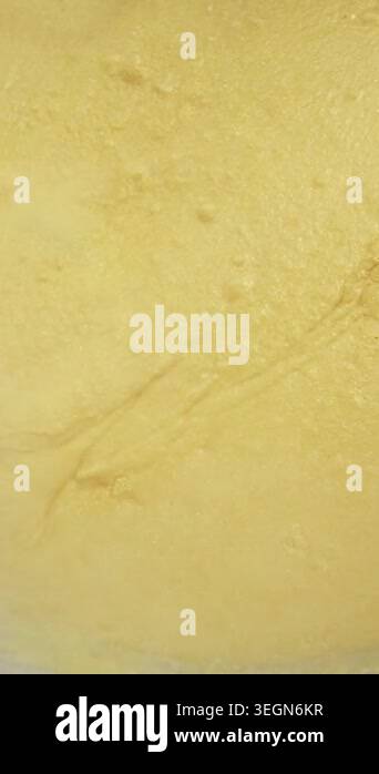 Yellow batter is mixed with a spatula in a clear bowl, highlighting the ...