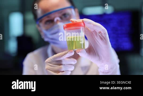 Woman scientist holds clear cup with yellow liquid in lab. Gloved hands ...
