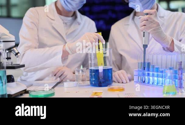 Women chemists wearing protective gear research blue liquid in lab ...