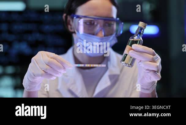 Woman scientist checks color strip near small vial. Gloved hands ...