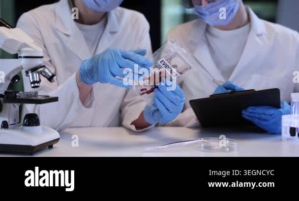 Women experts study dollar bill with red stains in plastic bag at desk ...