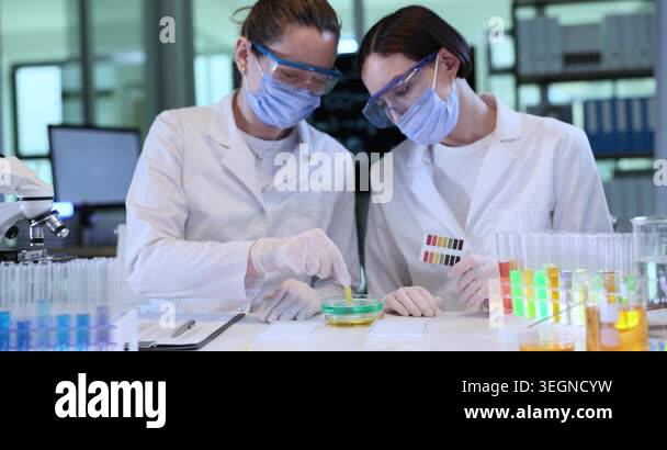 Women chemists conduct test of liquid pH with reagent and color scale ...