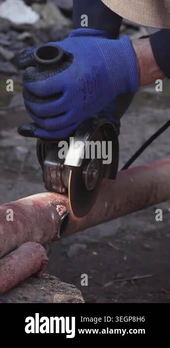 A worker uses an electric angle grinder to slice a rusted metal pipe ...