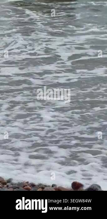 Powerful ocean waves surge and break around large, dark boulders ...