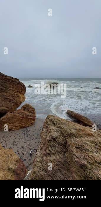Dynamic ocean waves roll onto a pebble beach, framed by weathered ...