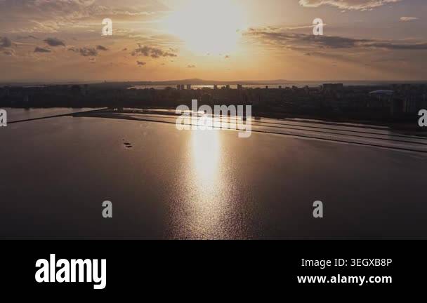 A sunset casts warm light over the city skyline. Water reflects the sun ...