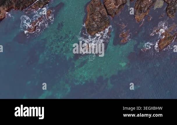 Water splashes against rocks along a coast. The water shows shades of ...