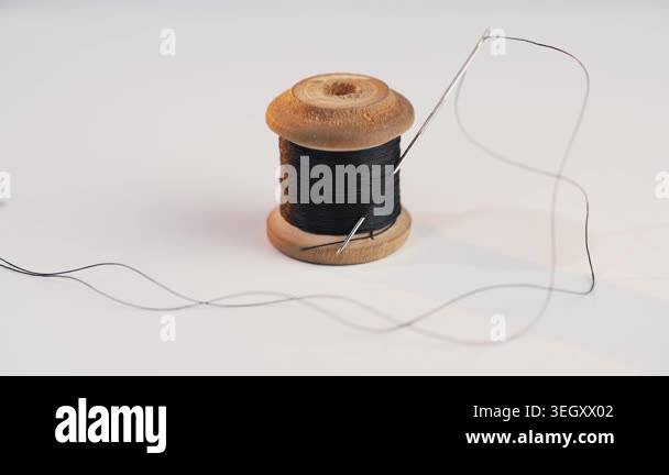 A sewing needle with a black thread inserted through its eye, placed on ...