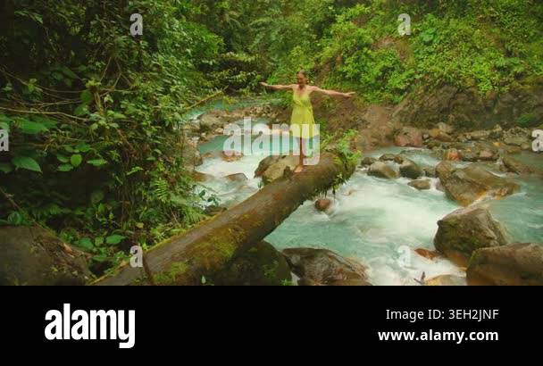 Tourist balancing on fallen log above vibrant Blue Falls river in Costa ...