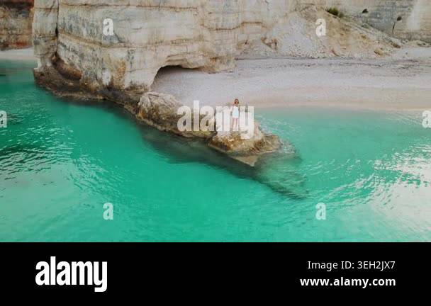 Traveler woman walking on offshore rock facing secluded turquoise cove ...
