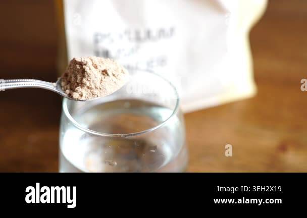 Psyllium husk powder being spooned into a clear glass of water and ...