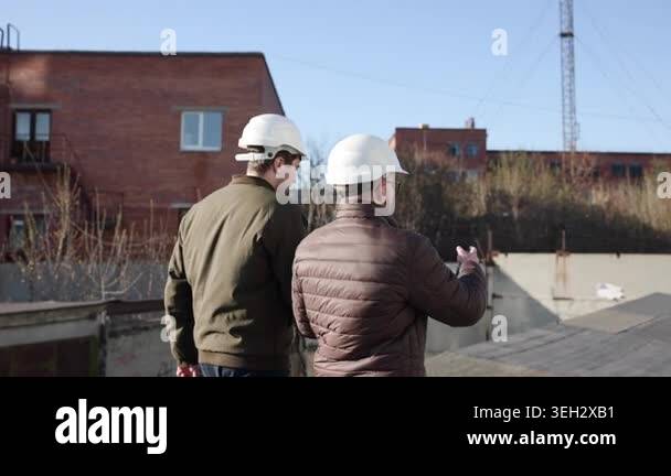 Two Inspectors Walking And Pointing Rooftop, Wearing White Helmets And ...
