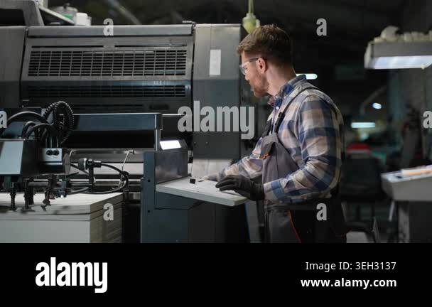 Focused male technician in safety glasses operating a large offset ...