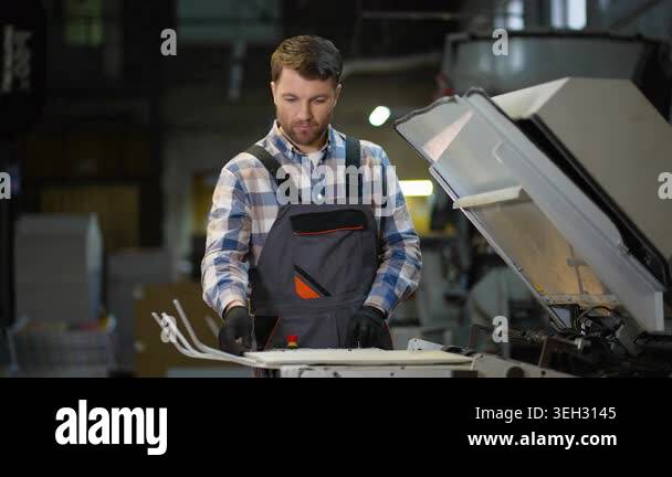 Male factory worker operating an industrial printing machine. Focused ...