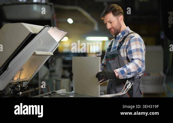 Male operator in uniform working at a printing plant, loading paper ...