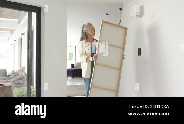 Entering hallway carrying canvas, woman is hanging grey abstract ... - Elegantly Minimalist Home Interior Inspiration