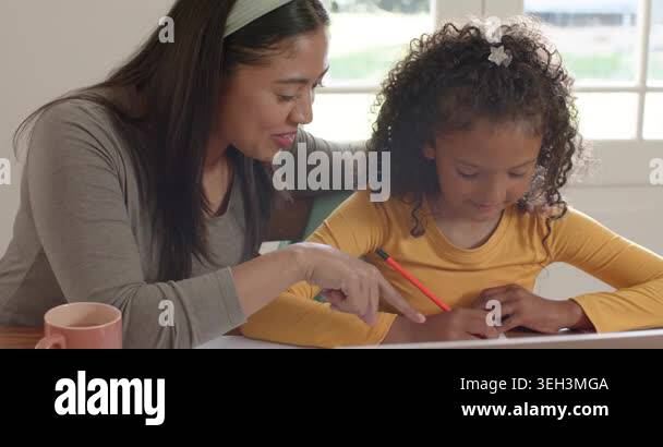 Diverse mother and daughter tracing letters numbers at home table ...