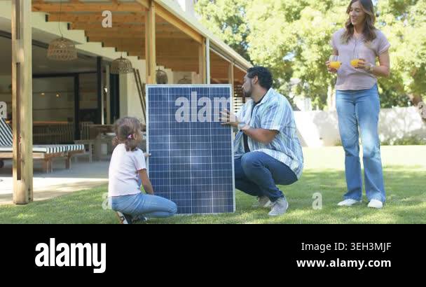 Family man crouching beside solar panel on lawn, pulling cables ...