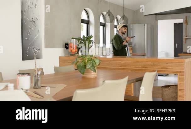 View of Indian man walking into kitchen, picking up remote, pressing buttons to ...