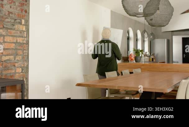 Image showcasing Man entering dining area carrying artwork panel, aligning edges against ...