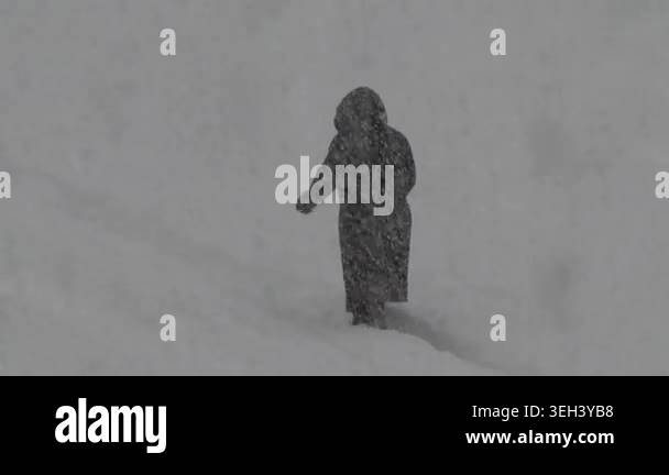 A person in a black coat walks alone through a heavy snowstorm ...