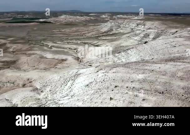 Pale badlands spread across a desert valley, revealing eroded gullies ...