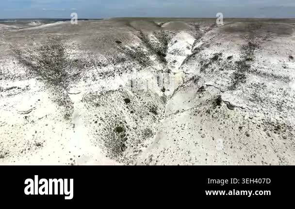 Pale badlands spread across a desert valley, revealing eroded gullies ...