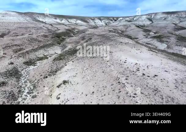 Pale badlands spread across a desert valley, revealing eroded gullies ...