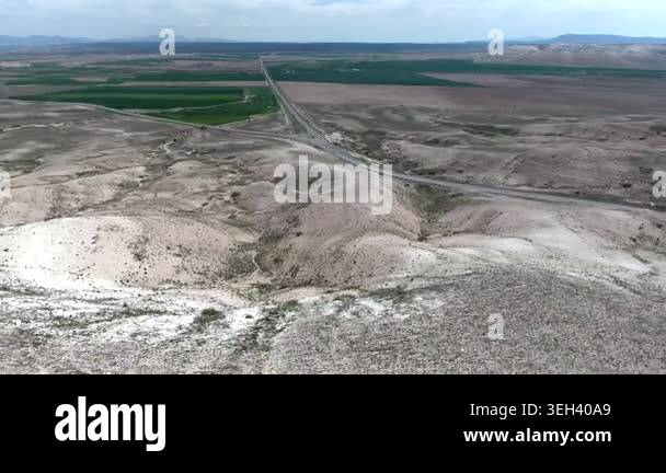 Pale badlands spread across a desert valley, revealing eroded gullies ...